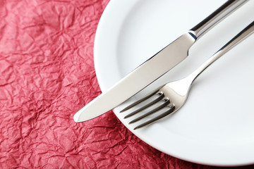 Fork, knife and plate on red background