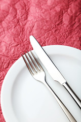 Fork, knife and plate on red background