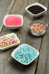 Colorful sprinkles in bow on grey wooden background