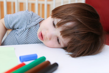 Tired little boy with felt pens rest his head on a table