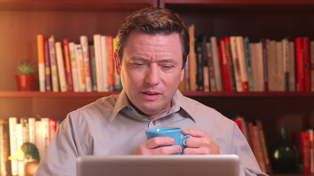 An upset man drinking coffee is video chatting on a computer