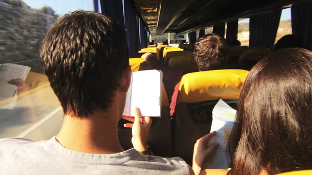 Over the shoulder shot of a young couple reading a book as they takes a bus ride.