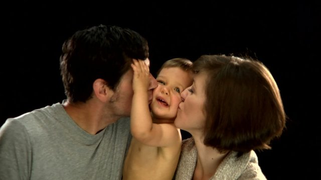 A mother and father hold their smiling new born son and hug and kiss him