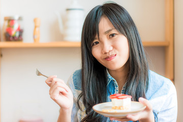 Smiling asian woman eating some strawberry cake in bakery cafe