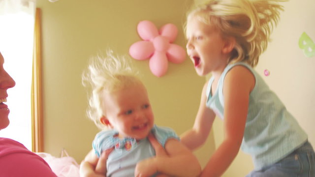 A young girl jumps on her bed as her mother and sister play next to her