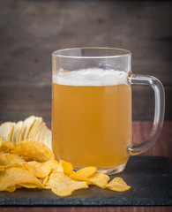 Beer with foam in glass mug and potato chips