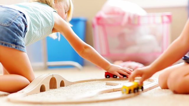 Two young girls sit on the floor and play with a wooden train set