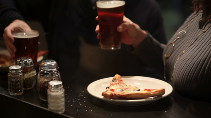 A couple cheering their beers over pizza in the city at night