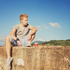 Fototapeta na wymiar Young man with takeaway coffee relaxing outdoors in summer 