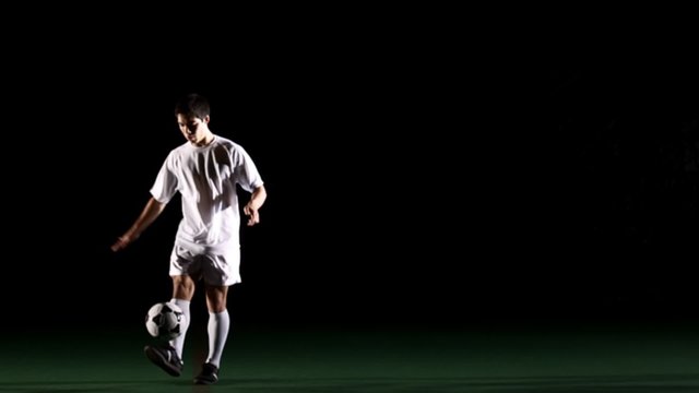 Isolated soccer player on black juggles a ball