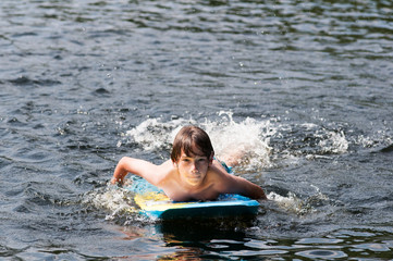 young boy swimming in a lake with a boogie board