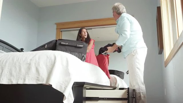 A man and woman unpack their bags which are resting on the bed