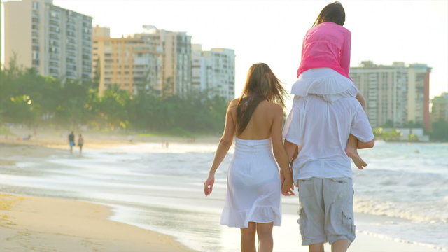 A family walks down the beach with the daughter on the father's shoulders