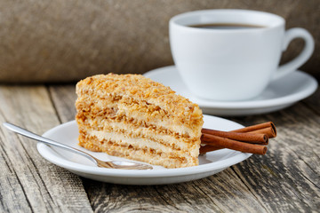 Tasty honey cake with cup of coffee on wooden background.