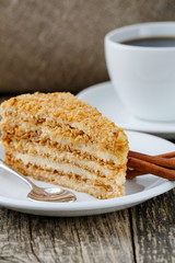Tasty honey cake with cup of coffee on wooden background.