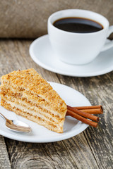 Tasty honey cake with cup of coffee on wooden background.