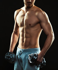 Fototapeta na wymiar Athletic attractive man with dumbbells on the black