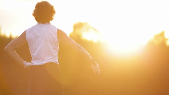 Female golfer tees off in the sunset. Medium shot.