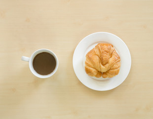 Croissant on white plate and cupof coffee.