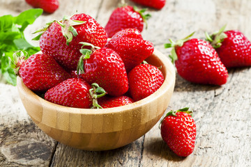 Fresh strawberries in a wooden bowl on a wooden table in rustic