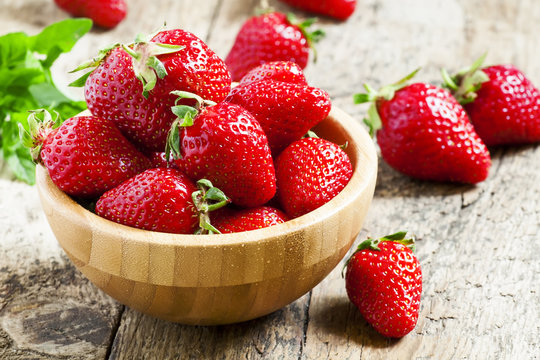 Fresh strawberries in a wooden bowl on a wooden table in rustic