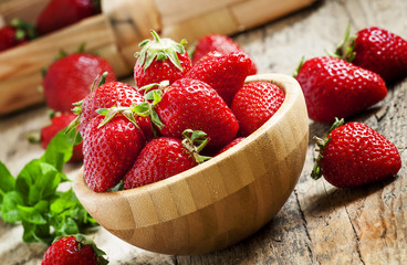 Fresh strawberries in a wooden bowl on a wooden table in rustic