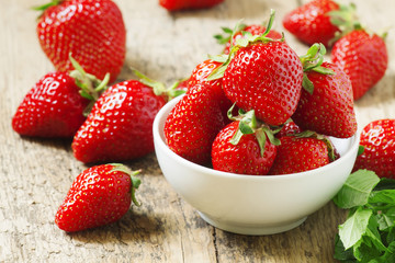 Fresh strawberries in a white porcelain bowl on wooden table in