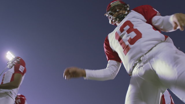 The camera looks up into a huddle full of football players talking before a play