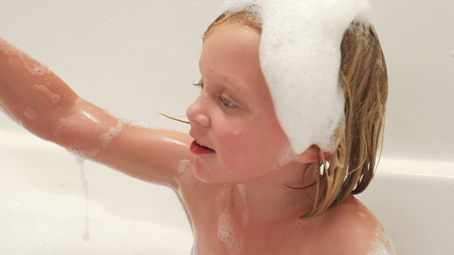 A little girl washes while a baby plays with a rubber ducky in a bubble bath