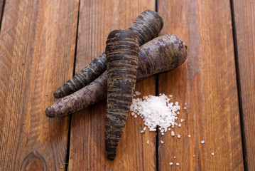 purple carrots with salt on raw wooden table