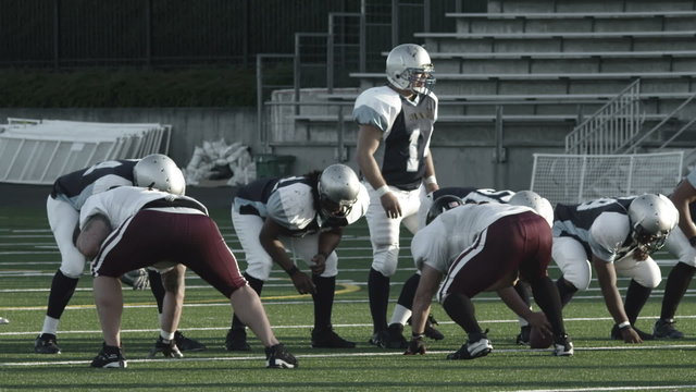 A quarterback stands at the line of scrimmage and prepares to hike the ball