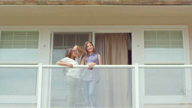 Close up of two sisters hugging and smiling as they stand on the balcony of their house