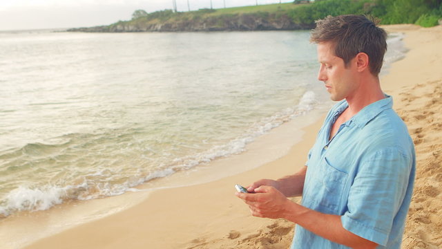 A man looks at his phone standing on the beach and takes a picture of the ocean