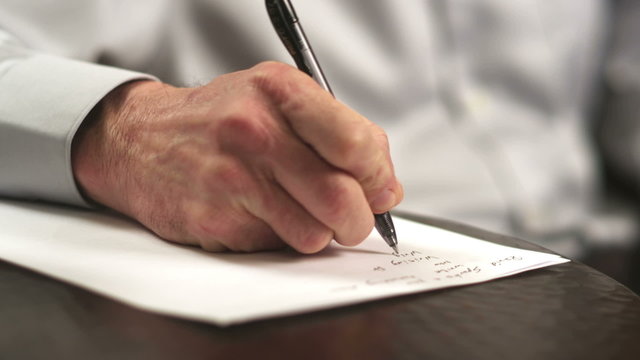 A man in a dress shirt takes handwritten notes after he uses a touchscreen tablet computer in a coffee shop