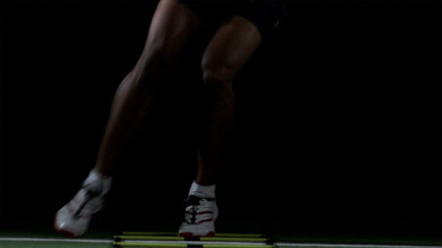 A African American male athlete trains on a speed latter across turf