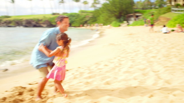 A young girl runs down the sand and jumps into his dad's arms