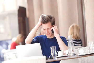 Young Man Sitting in Outside Coffeehouse Talking on Phone