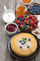 crepes, fresh berries and jams on wooden table, vertical