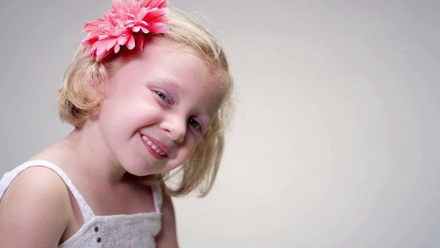 Little girl with make-up and flower in her hair smiles against white background