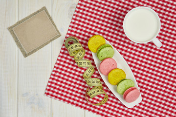 Empty plate with measure tape, macarons and milk. Diet food on w