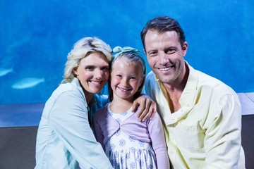 Obraz premium Happy family looking at camera beside the fish tank