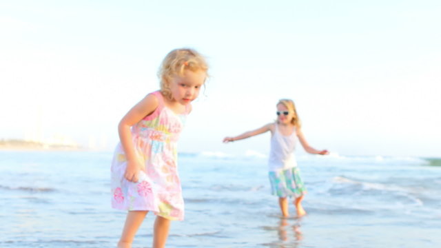 Two young girls run into the water at the beach and back out