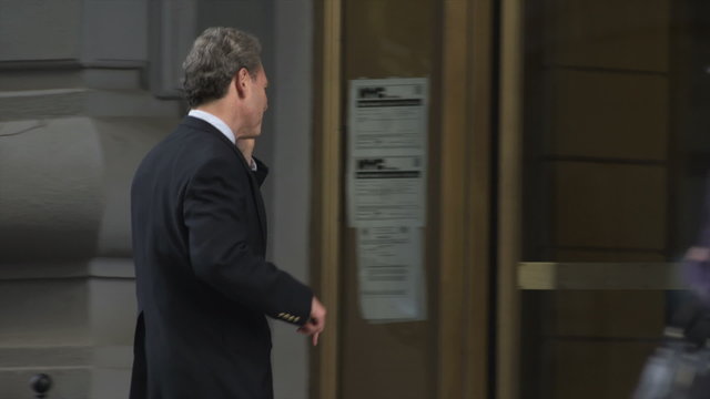 A businessman is already working via a cell phone when he gets to his building