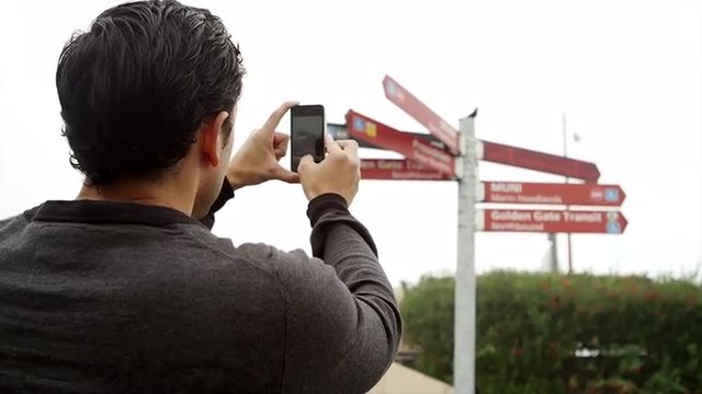A man takes a picture of signs in the golden gate bridge park on a foggy day