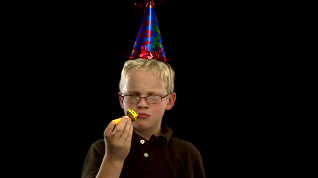 A young blond boy wears a party hat and blows a noise maker