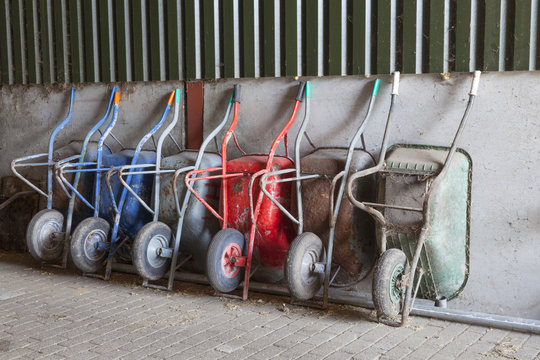 six wheelbarrows rest against wall of farm barn