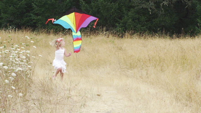 A cute little girl runs toward the camera with a big kite. 