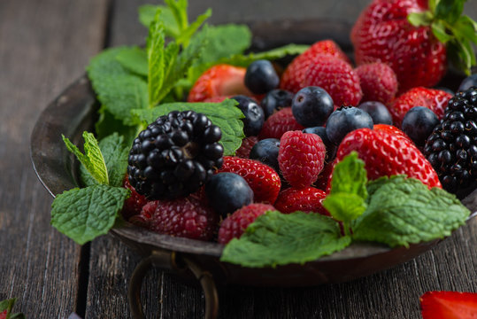 Fresh summer berries with mint in rustic bowl