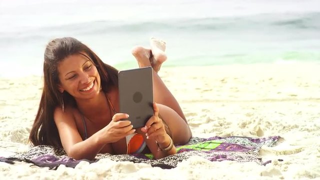 Brazilian woman uses a tablet on the beach