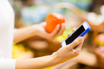woman with smartphone and persimmon in market